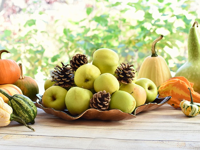 Fall table settings with pumpkins on a rustic table and a bowl full of granny smith apples and pinecones.